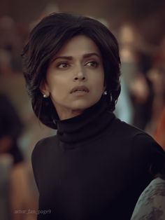 a woman with dark hair and black turtle neck top looking at something in the distance