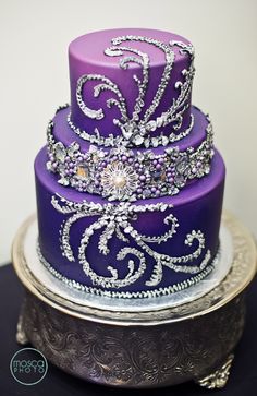 a three tiered purple cake with white and silver designs on it's sides