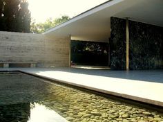 the exterior of a modern house next to a pool with rocks on it and trees in the background