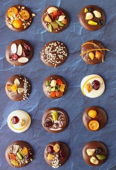 chocolate donuts with different toppings are arranged on a blue tablecloth and laid out in rows