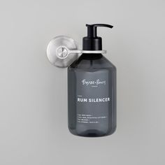 a soap dispenser hanging from a hook on a gray wall with a black bottle