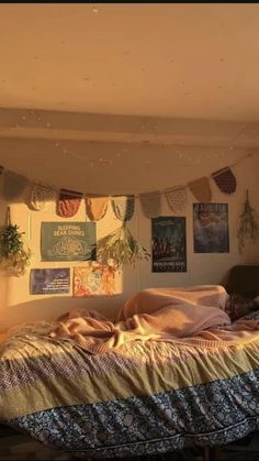 an unmade bed in a room with posters on the wall and plants hanging above it