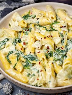 a white bowl filled with pasta and spinach on top of a blue table cloth