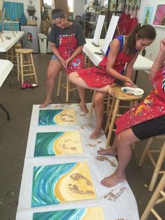 three people sitting at a table with paintings on it