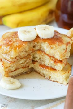 a stack of pancakes with bananas and syrup on a white plate next to a knife