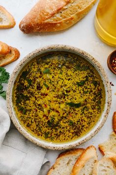 a bowl filled with pesto and bread on top of a white tablecloth next to some sliced baguettes