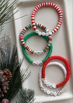 three bracelets sitting on top of a white tray next to pine cones and christmas decorations