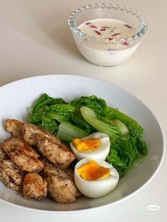 a white plate topped with meat and veggies next to a bowl of dressing