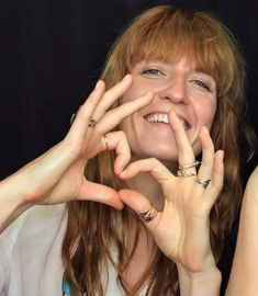 a woman making the shape of a heart with her hands and smiling at the camera