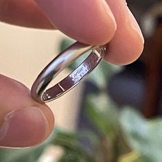 a close up of a person's hand holding a silver ring with writing on it