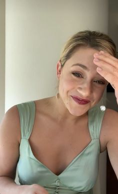 a woman sitting in front of a mirror with her hand on her head and looking at the camera