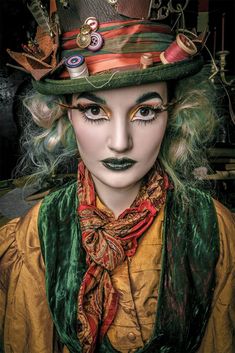 a woman with green hair wearing a top hat and scarves on her face,