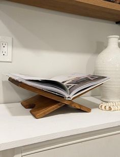 an open book sitting on top of a wooden shelf next to a vase and telephone