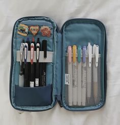 an open blue case filled with pens and pencils on top of a white sheet