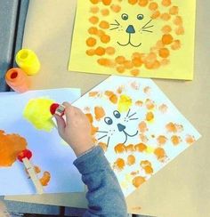 a child's hand holding a paintbrush and painting on paper with lion faces