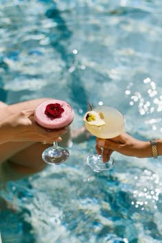 two people holding wine glasses in their hands near a swimming pool with water and bubbles