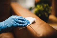 a person in blue gloves cleaning a couch with a microfiber cloth on it