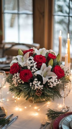 a centerpiece with red roses and white lilies on a dining room table set for christmas