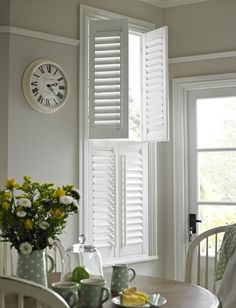 a clock on the wall above a table with flowers and cups in front of it