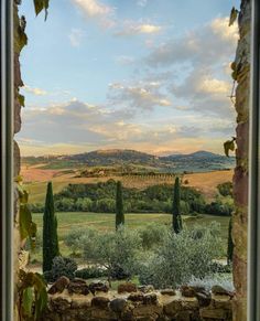 an open window looking out onto a field and hills with trees in the foreground