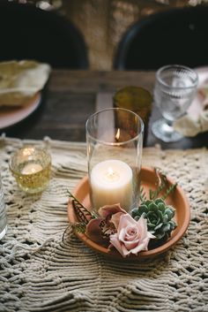 an arrangement of flowers and candles on a table with lace doily around the place setting