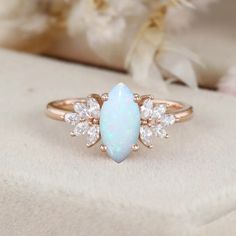 an opal and diamond ring sits on top of a white cloth with flowers in the background