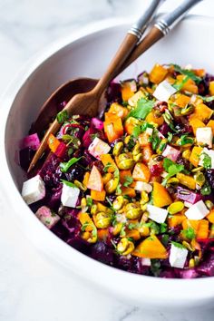 a white bowl filled with salad and two wooden spoons