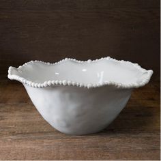 a white bowl with scalloped edges on a wooden table, ready to be used as a centerpiece