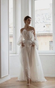 a woman standing in front of a window wearing a white dress