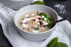 two white bowls filled with soup and topped with spinach leaves, mushrooms and sour cream