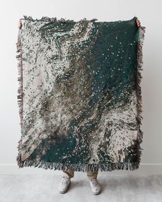 a person holding up a green and white blanket with silver stars on the top, while standing in front of a white wall