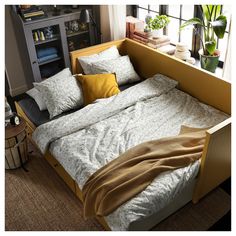 a bed with two pillows on top of it next to a book shelf and potted plants