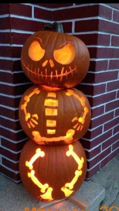 three pumpkins stacked on top of each other in front of a brick wall with glowing eyes