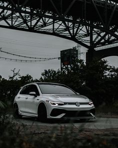 a white car parked under an overpass in front of some trees and power lines