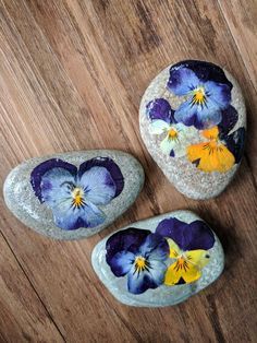 three rocks with flowers painted on them sitting on a wooden floor next to each other