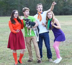 three people and a dog posing for a photo in a field with trees behind them