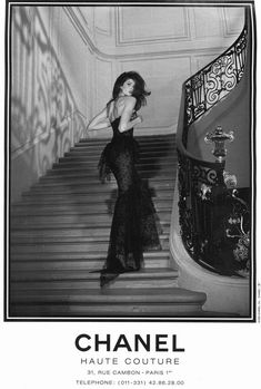 a black and white photo of a woman in a dress standing on the stairs with her hair blowing in the wind