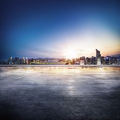 an empty parking lot with the sun setting in the background and city lights reflected on the ground