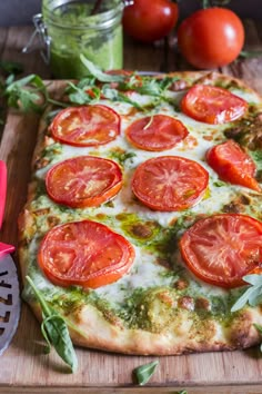 a pizza sitting on top of a cutting board covered in cheese and toppings next to tomatoes