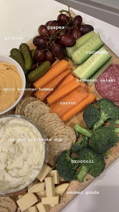 a platter with cheese, crackers, broccoli, grapes, cucumbers and carrots