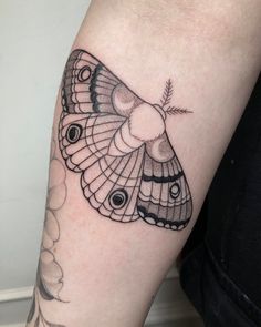 a black and white butterfly tattoo on the left arm, with an arrow in it's center