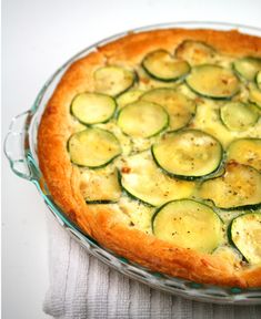 a pie with zucchini and cheese on top is sitting on a white table