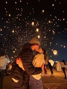 a man and woman kissing in front of many floating paper lanterns at the night sky