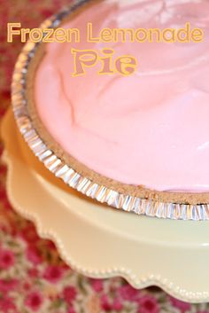 a frozen lemonade pie sitting on top of a cake plate with pink frosting