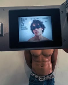 a shirtless man holding up a video camera