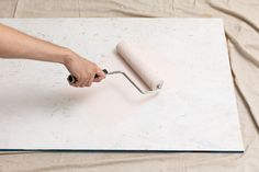 a person using a roller to paint a piece of white paper on a sheet of cloth