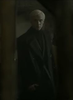 a man in a black suit and white hair is looking at his reflection in the mirror