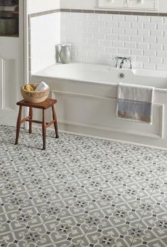 a white bath tub sitting next to a wooden stool in front of a tiled floor