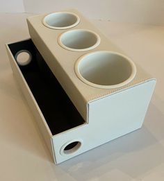 a white and black box with three cups in it on a table next to a cup holder