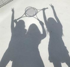 two women holding tennis racquets on top of a tennis court in shadow